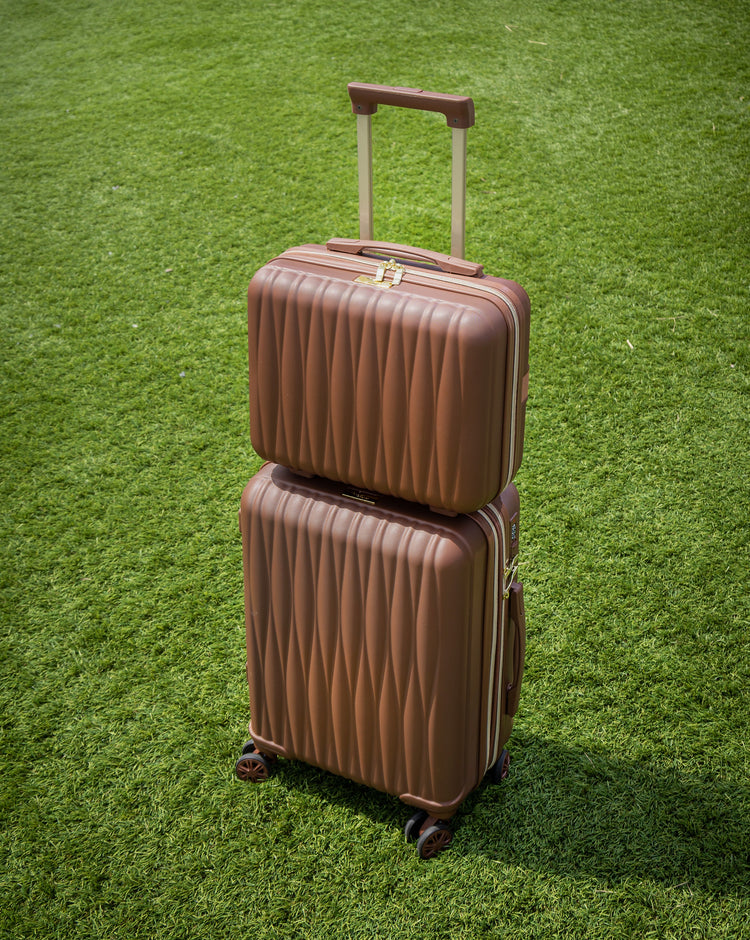 Two brown suitcases stacked on a grassy field