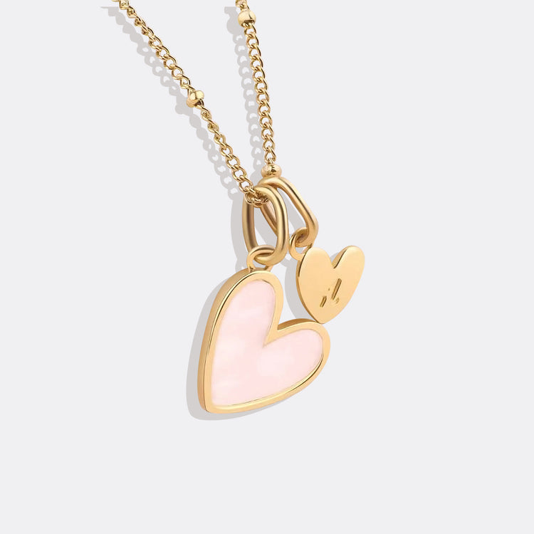 Gold necklace with a pink heart pendant on a light gray background