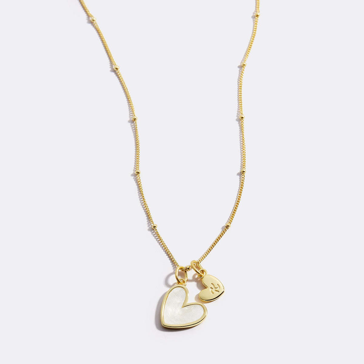 Gold necklace with a heart-shaped pendant on a light gray background
