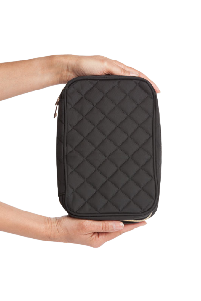 Black quilted travel case held by a person on a white background