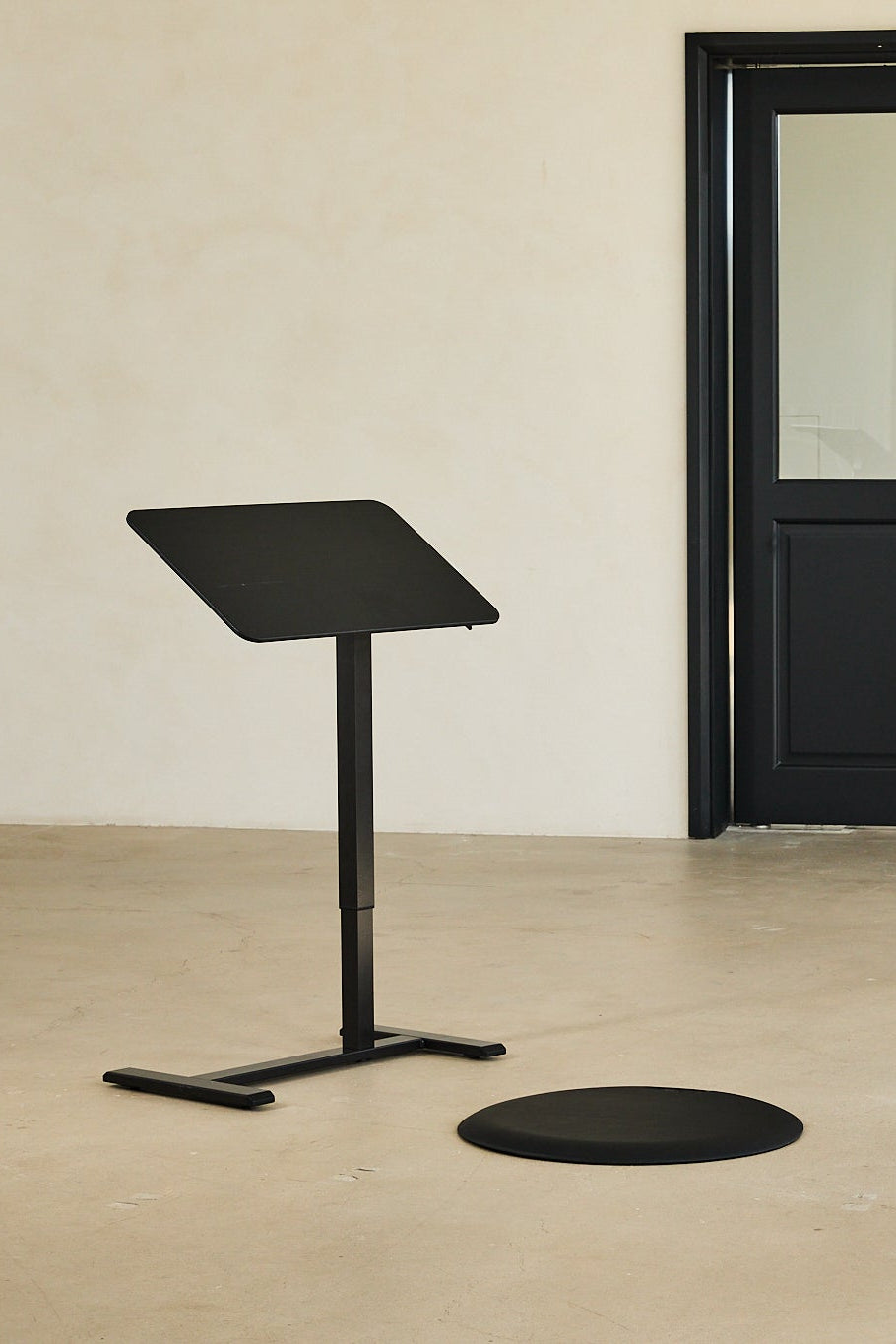Black adjustable stand against a beige wall with a black door.