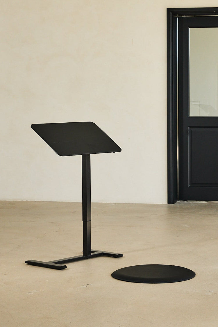Black adjustable stand against a beige wall with a black door.