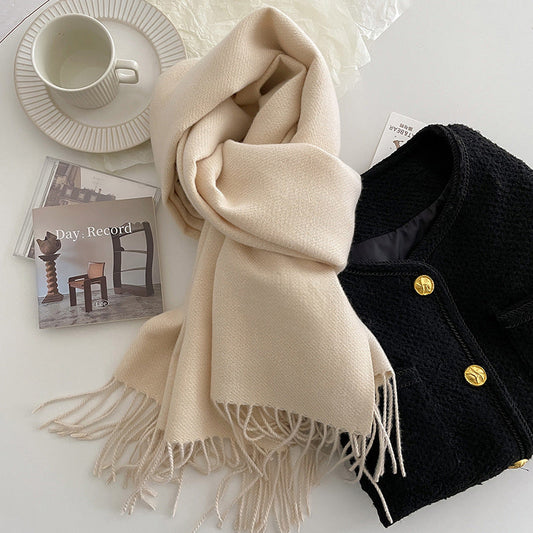 Beige scarf with tassels on a white surface with a black jacket and cup.