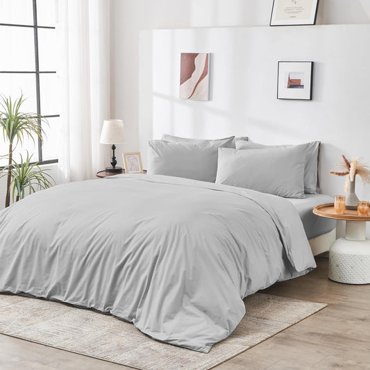 Gray bedding set on a bed in a well-lit bedroom with decor elements.