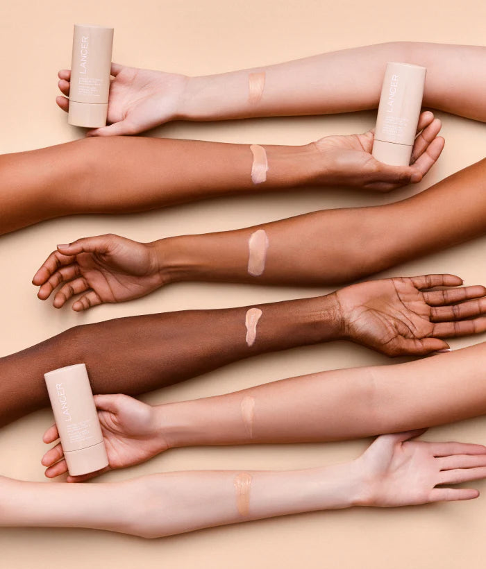 Multiple arms with different skin tones holding a cosmetic product on a beige background