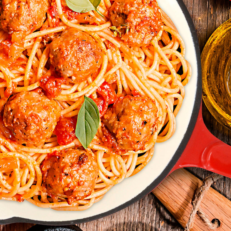 Spaghetti with meatballs in a red pan on a wooden surface
