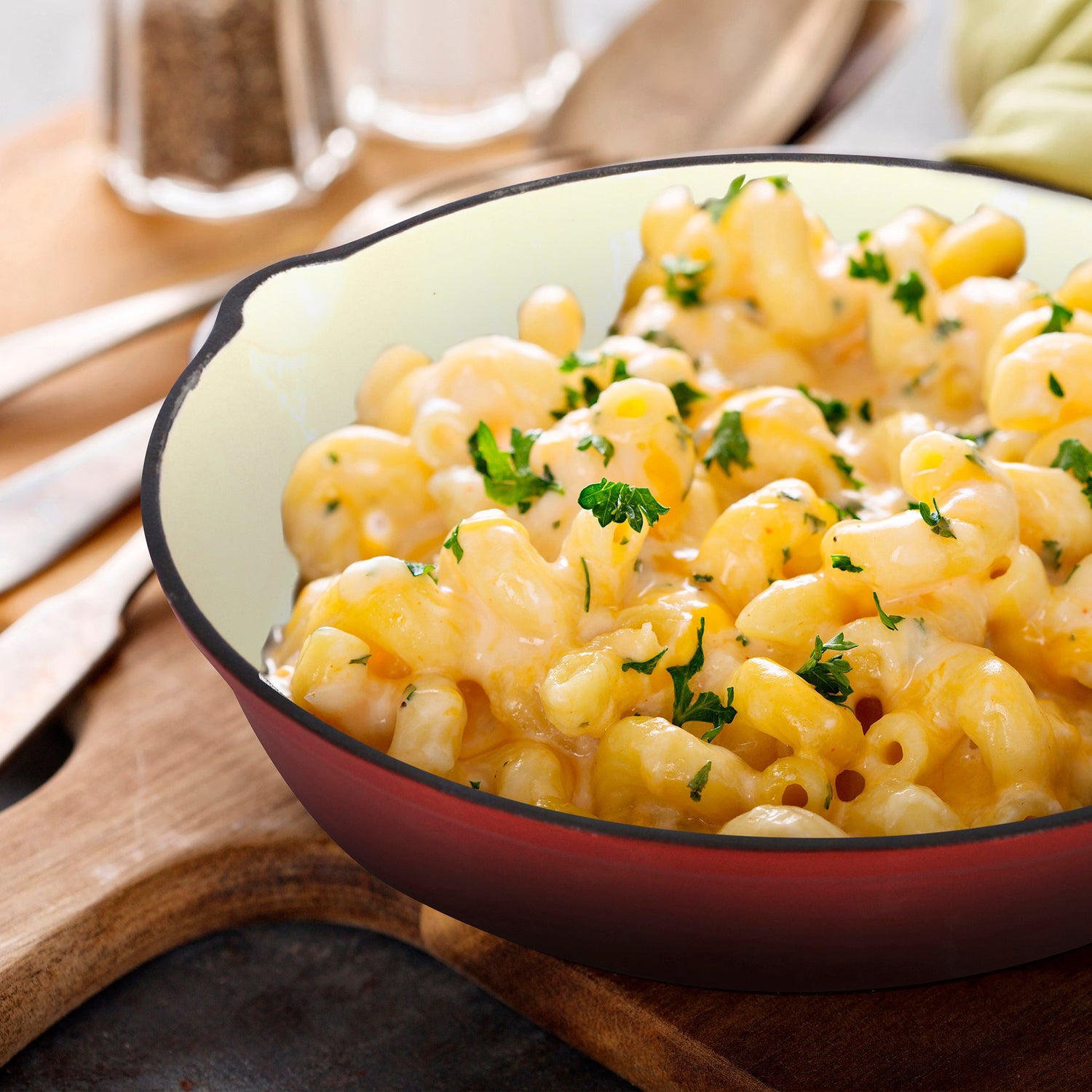 Macaroni and cheese with herbs in a red skillet on a wooden surface