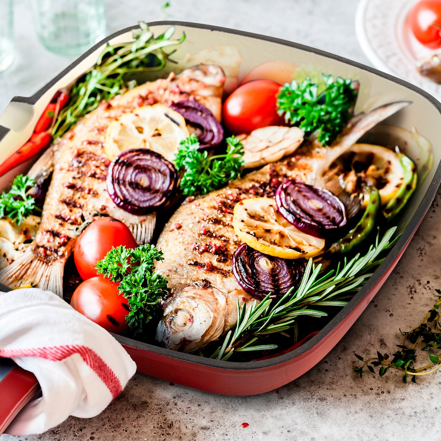 Baked fish dish with vegetables in a red baking dish on a stone surface.