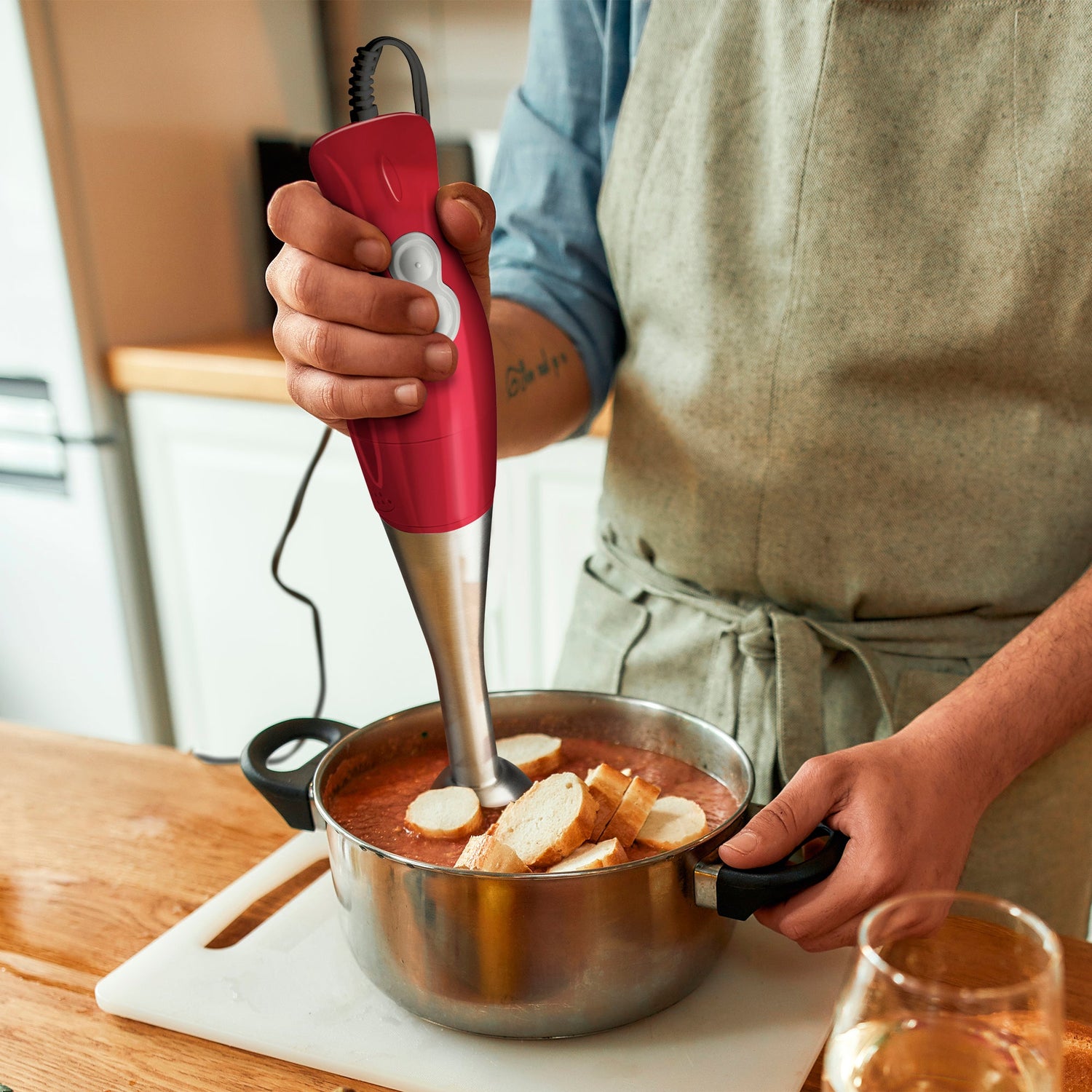 Person using a red immersion blender in a kitchen