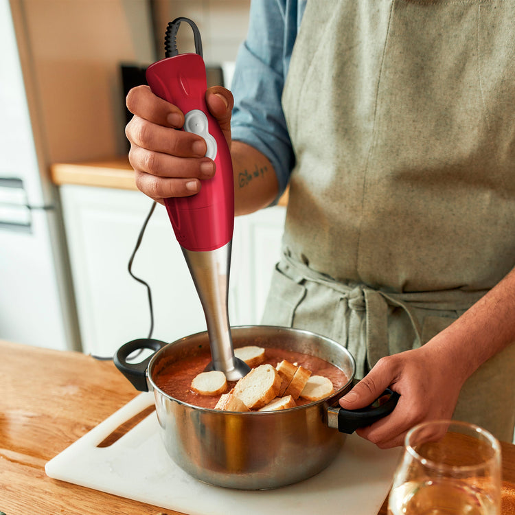 Person using a red immersion blender in a kitchen