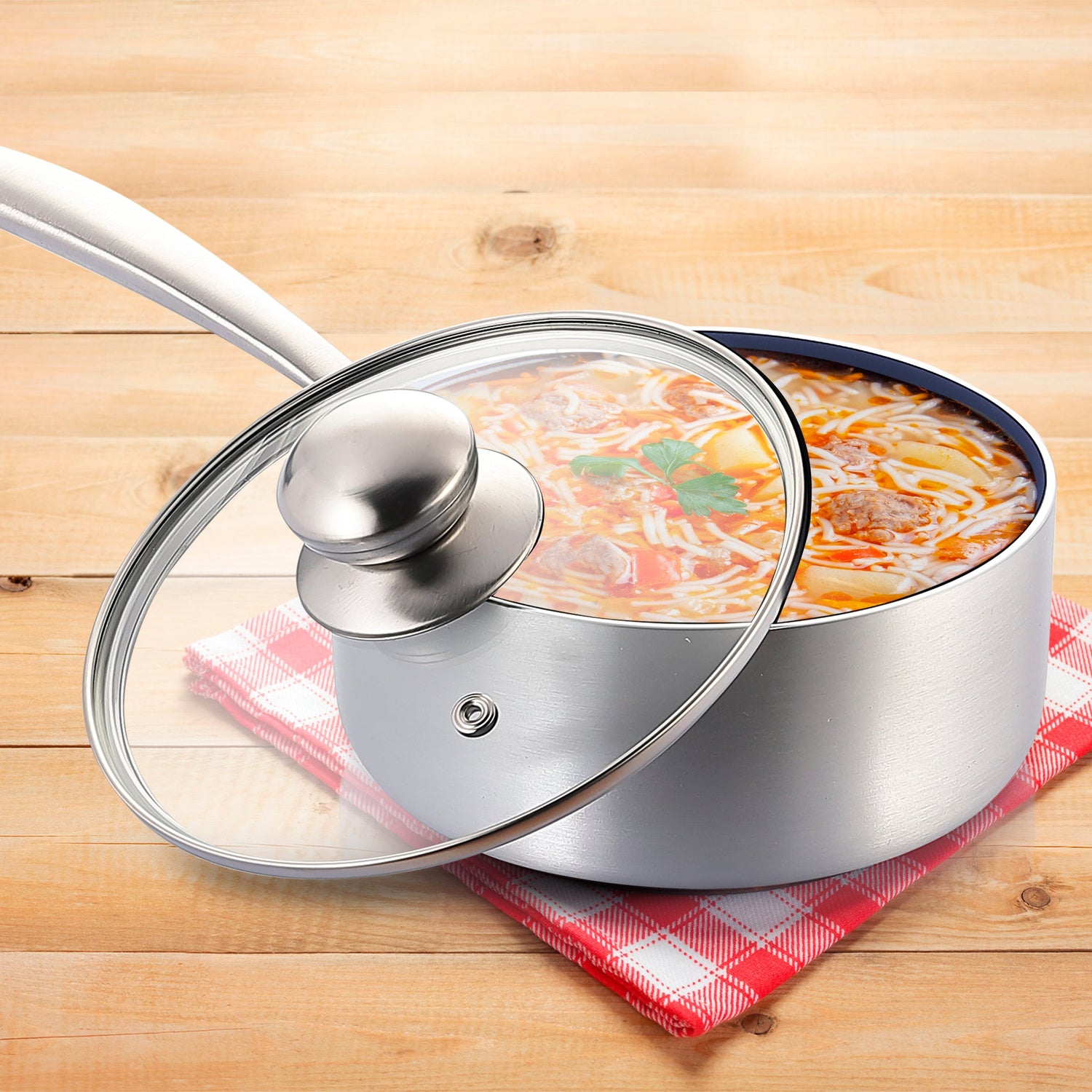 Stainless steel pot with glass lid containing a dish on a wooden surface