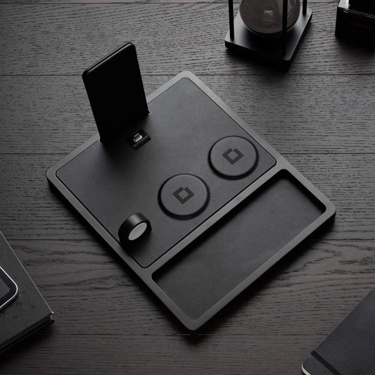 A black 4-in-1 MagSafe wireless charging station with separate sections for charging an iPad, Apple Watch, and other devices, displaying LED indicators.