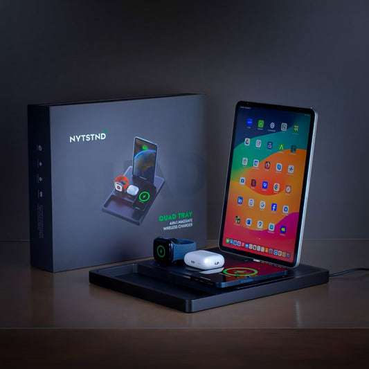 A black 4-in-1 MagSafe wireless charging station with separate sections for charging an iPad, Apple Watch, and other devices, displaying LED indicators.
