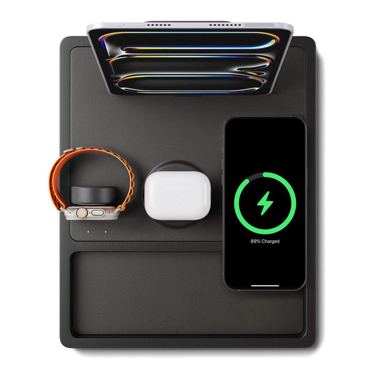 A black 4-in-1 MagSafe wireless charging station with separate sections for charging an iPad, Apple Watch, and other devices, displaying LED indicators.