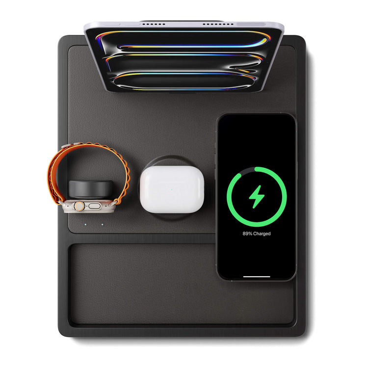 A black 4-in-1 MagSafe wireless charging station with separate sections for charging an iPad, Apple Watch, and other devices, displaying LED indicators.