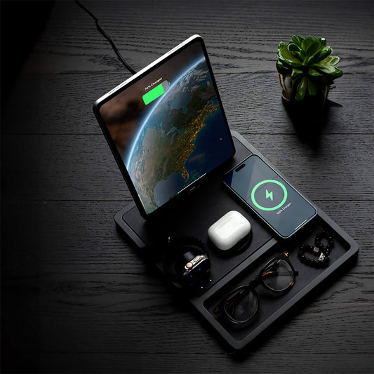 A black 4-in-1 MagSafe wireless charging station with separate sections for charging an iPad, Apple Watch, and other devices, displaying LED indicators.