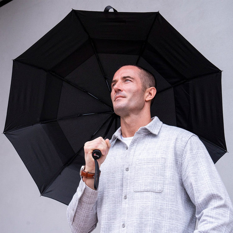 Man holding a large black umbrella against a gray background