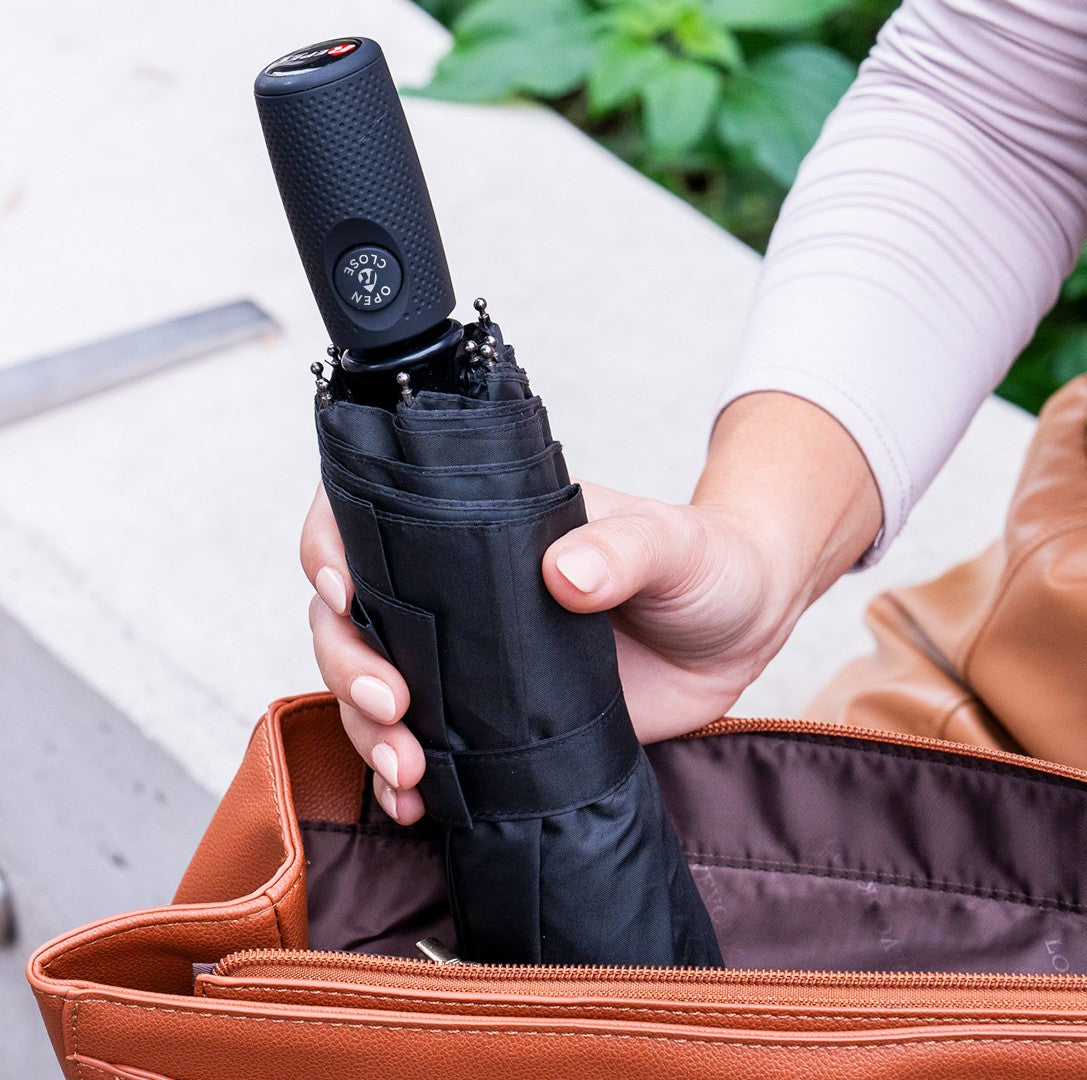 Person holding a black umbrella with a brown leather bag in the background