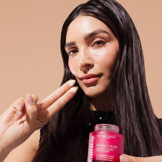 Christian Siriano Runway Radiance Ready Growth Factor Moisturizer, hydrating and glow-finish formula for all skin tones, shown in pink jar held by model applying product.
