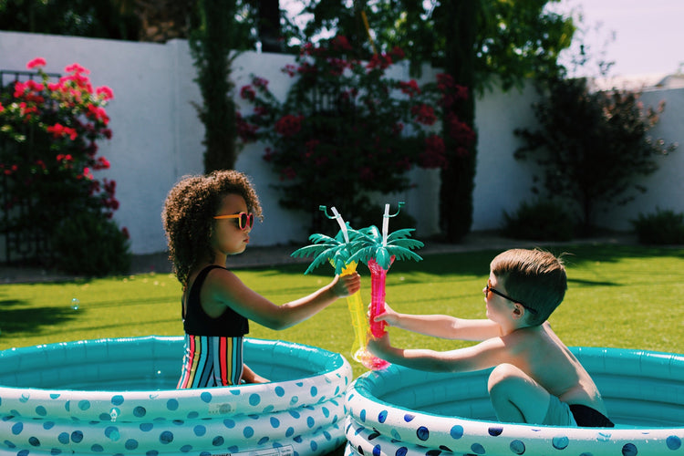 Two children playing with a toy palm tree in inflatable pools outdoors.
