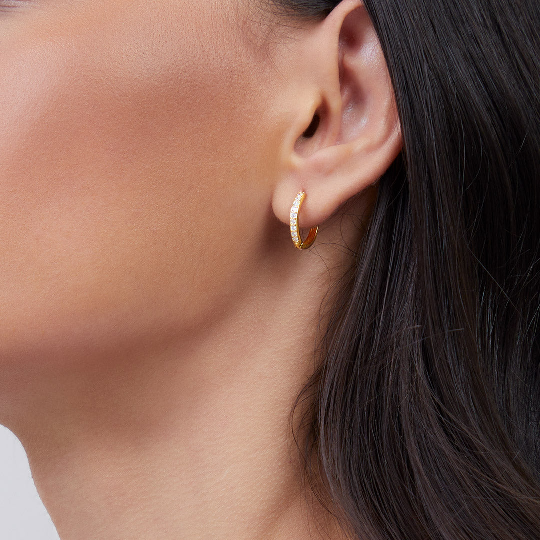 Close-up of a person wearing a gold hoop earring with dark hair and skin.