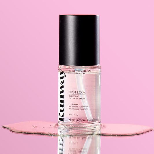 Christian Siriano Runway First Look Gripping Glow Primer in a clear bottle with black cap, displayed on reflective surface against a pink background.