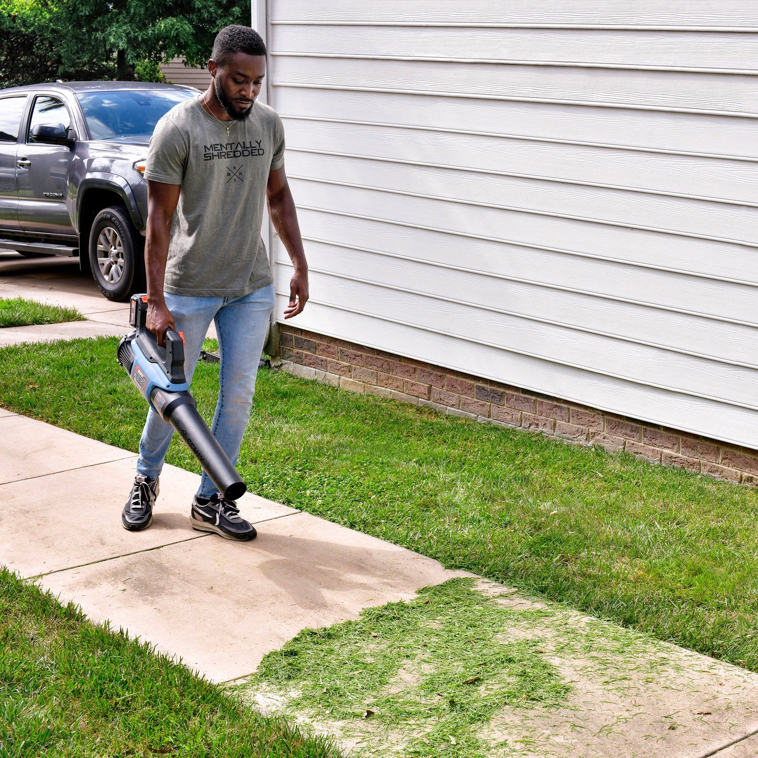Man using a leaf blower on a sidewalk next to a house