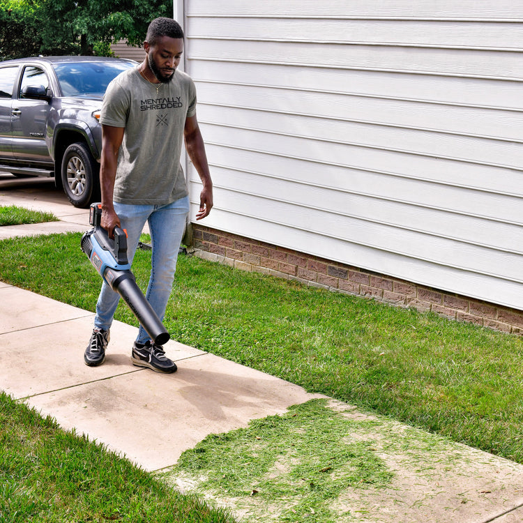 Man using a leaf blower on a sidewalk next to a house