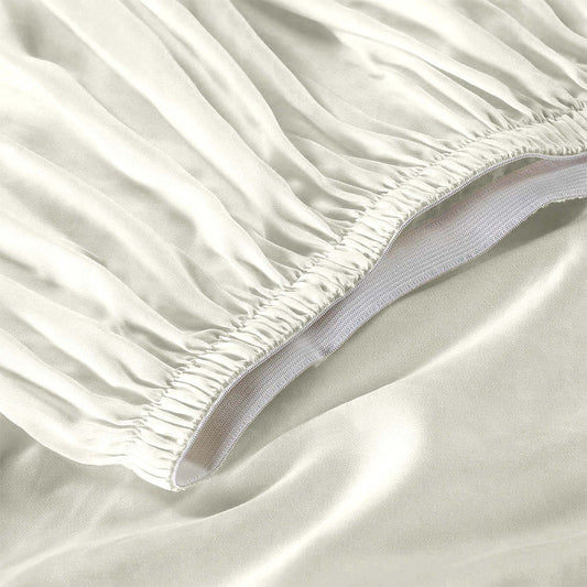 Neatly made bed with white bedding in a room with large windows and wooden furniture.