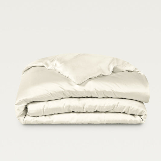 Beige bedding set with pillows on a bed in a room with large windows.