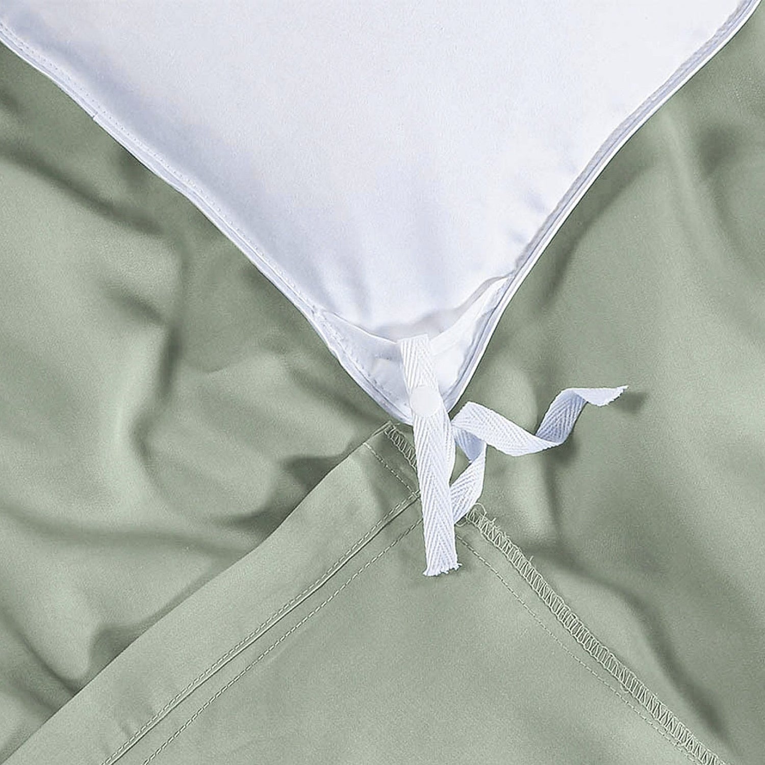 Close-up of a green fabric with a white pillow and tie, possibly from a bed or mattress cover.