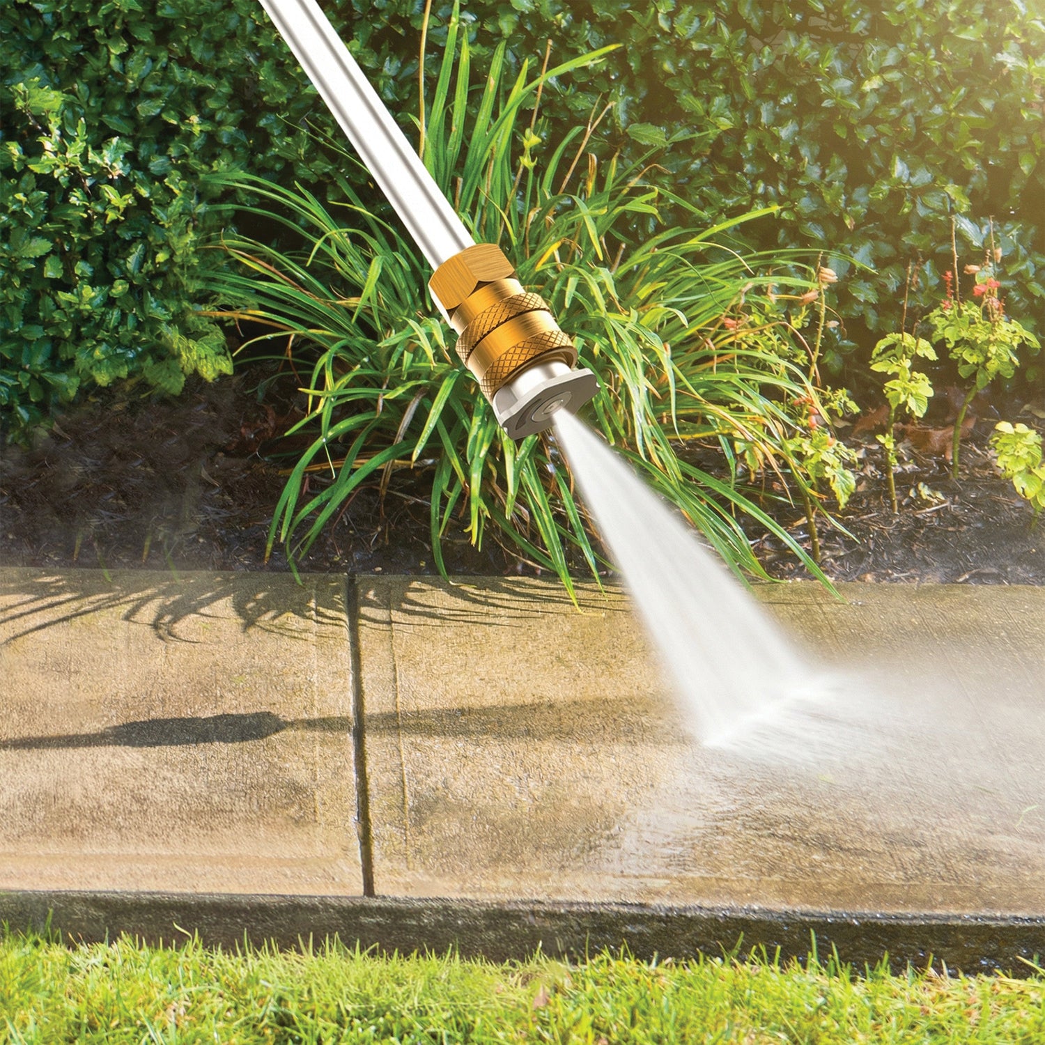 Hose nozzle spraying water onto a concrete surface with greenery in the background