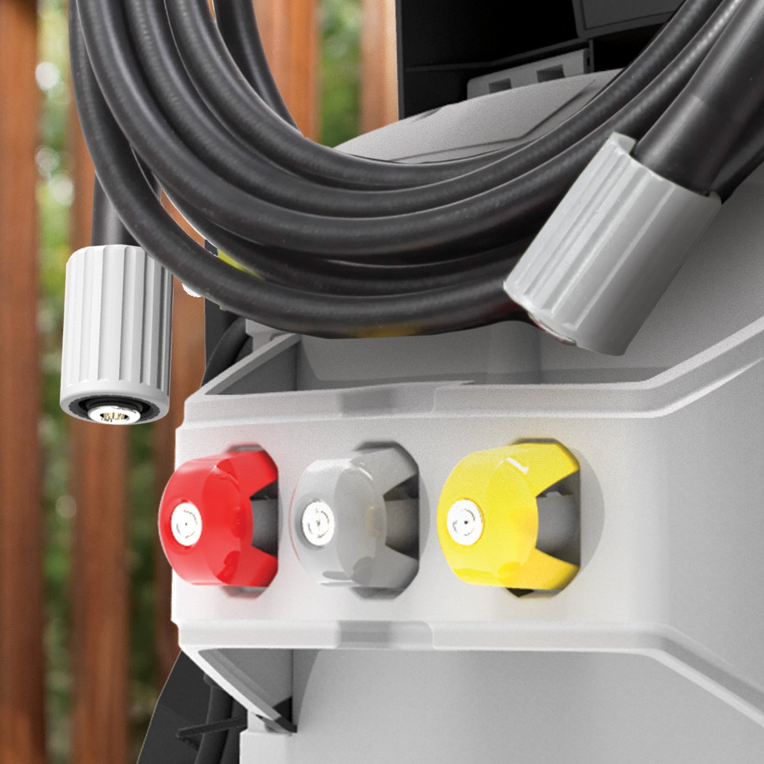 Close-up of a pressure washer with three control knobs in red, gray, and yellow, against a blurred outdoor background.