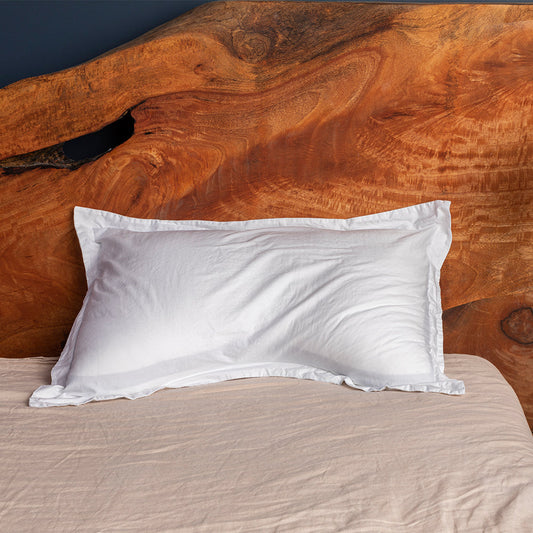 A white, rectangular side sleeper pillow with a pillowcase on a bed, against a wooden headboard background.