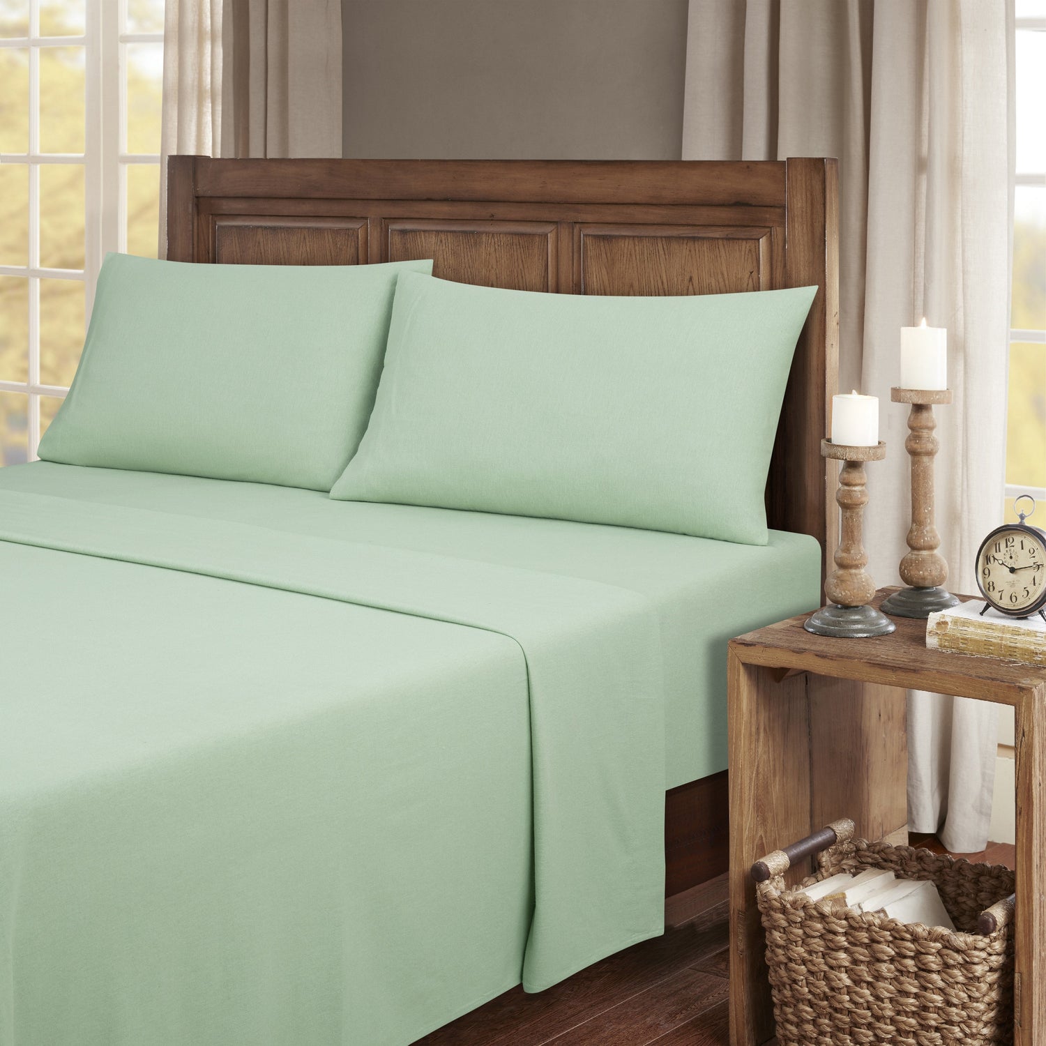Green bed sheets on a bed with a wooden headboard and side table in a bedroom setting.