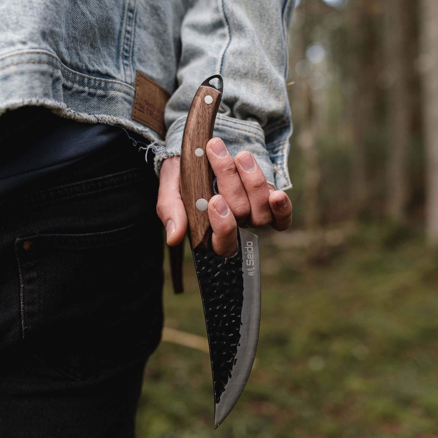 Person holding a knife with a wooden handle in a forest setting