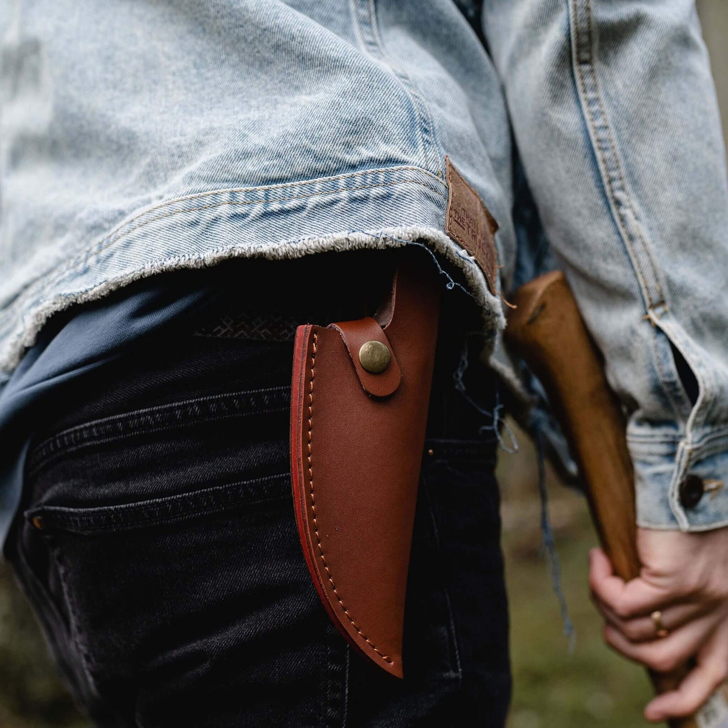 Person holding a rifle with a brown leather scabbard, wearing a denim jacket.