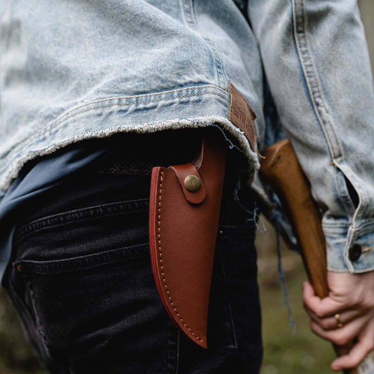 Person holding a rifle with a brown leather scabbard, wearing a denim jacket.