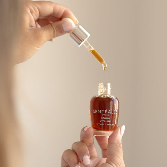 Hand holding a Senteless skincare serum bottle with dropper against a neutral background