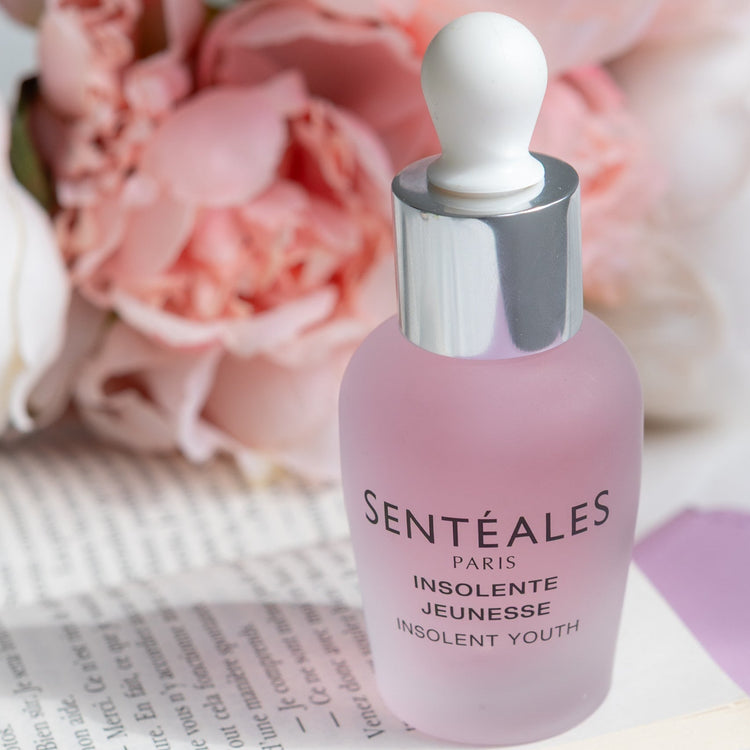 Pink serum bottle with silver cap on a book with pink flowers in the background