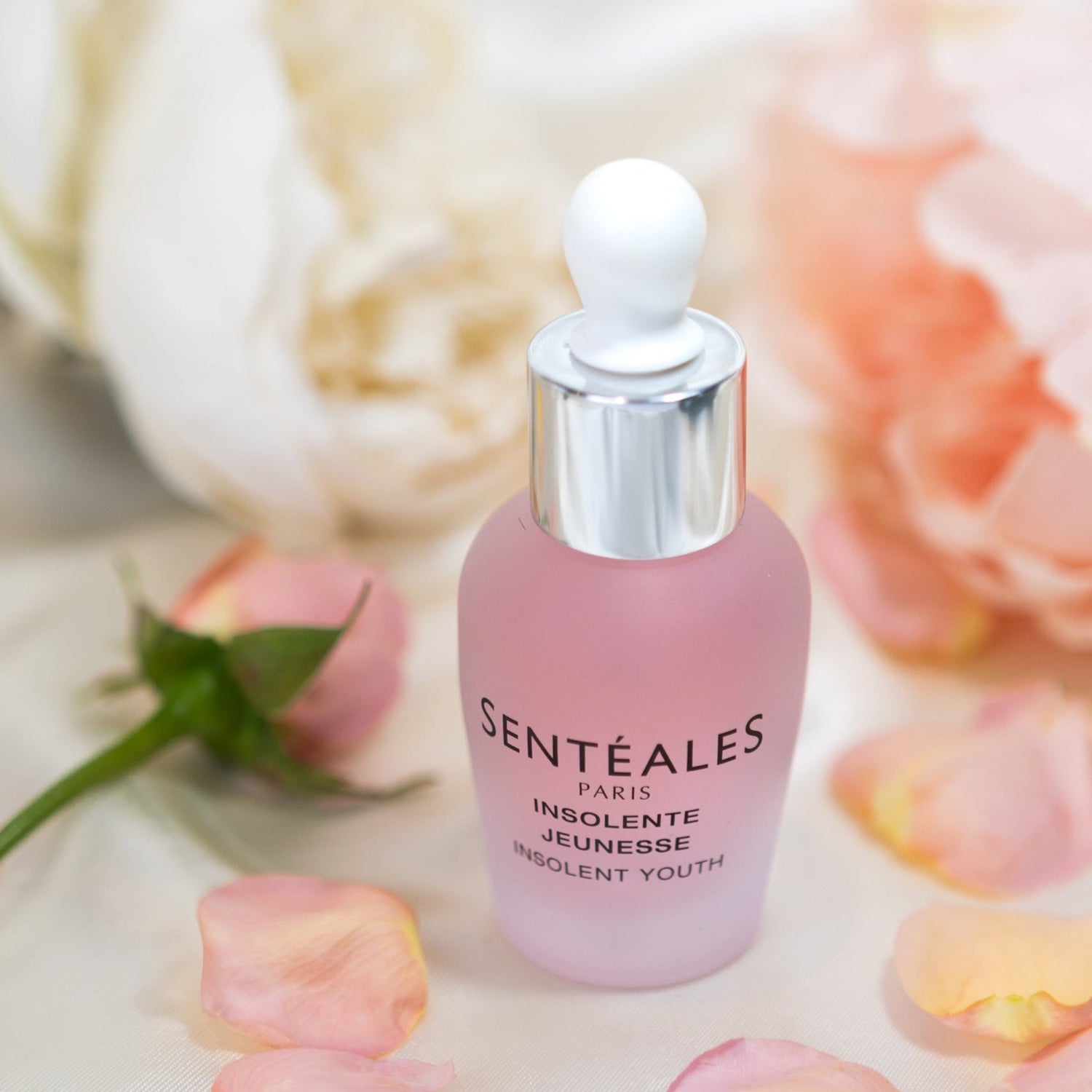 Pink skincare serum bottle with dropper labeled 'Senteales' on a soft floral background