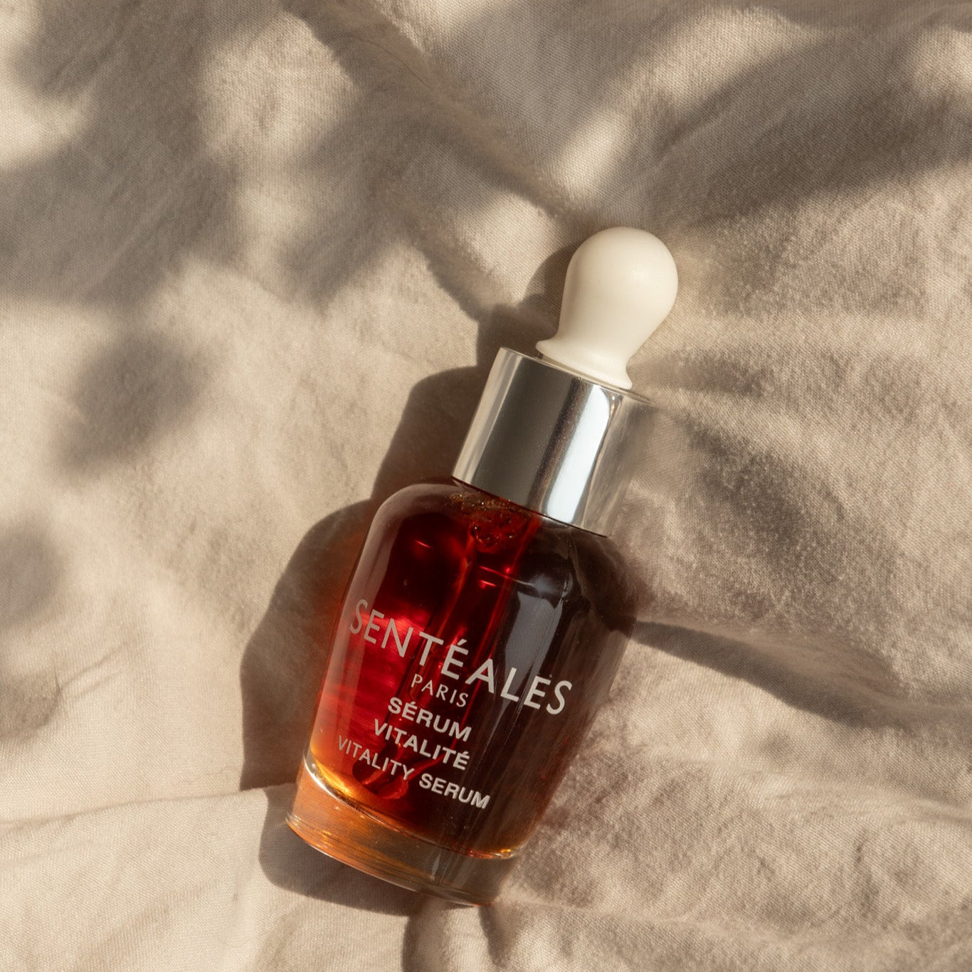 Serum bottle with 'Senteales' branding on a textured beige surface
