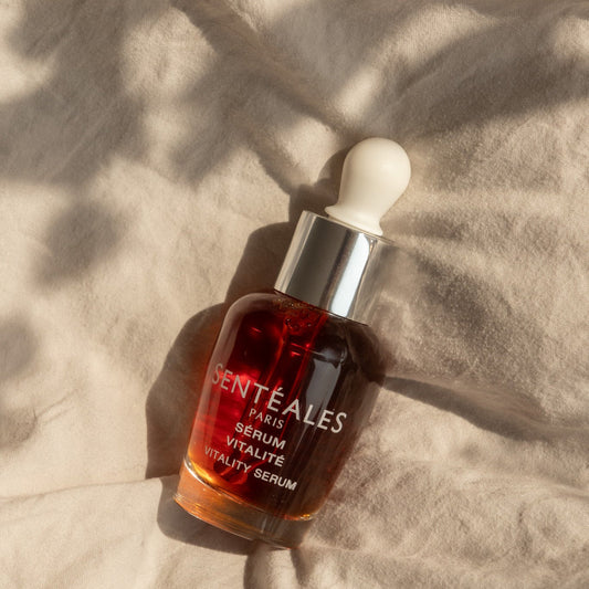 Hand holding a Senteless skincare serum bottle with dropper against a neutral background