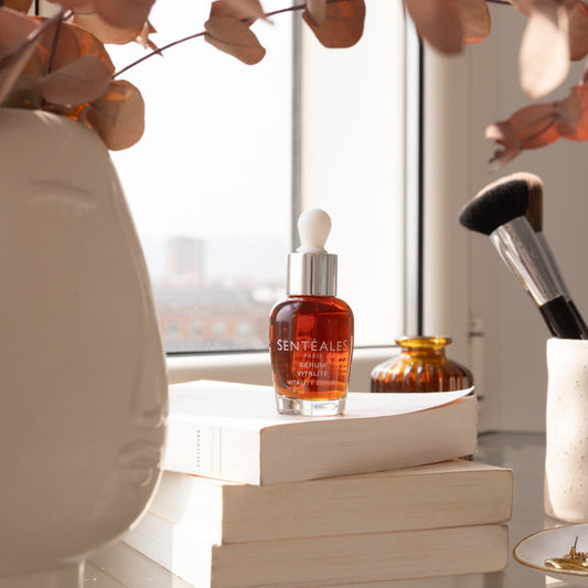 Hand holding a Senteless skincare serum bottle with dropper against a neutral background