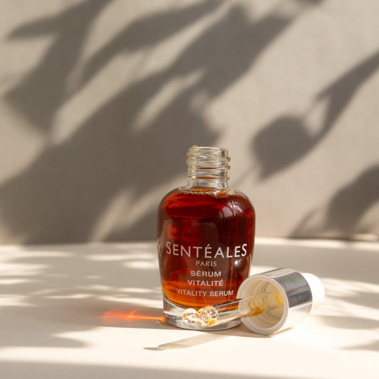 Hand holding a Senteless skincare serum bottle with dropper against a neutral background