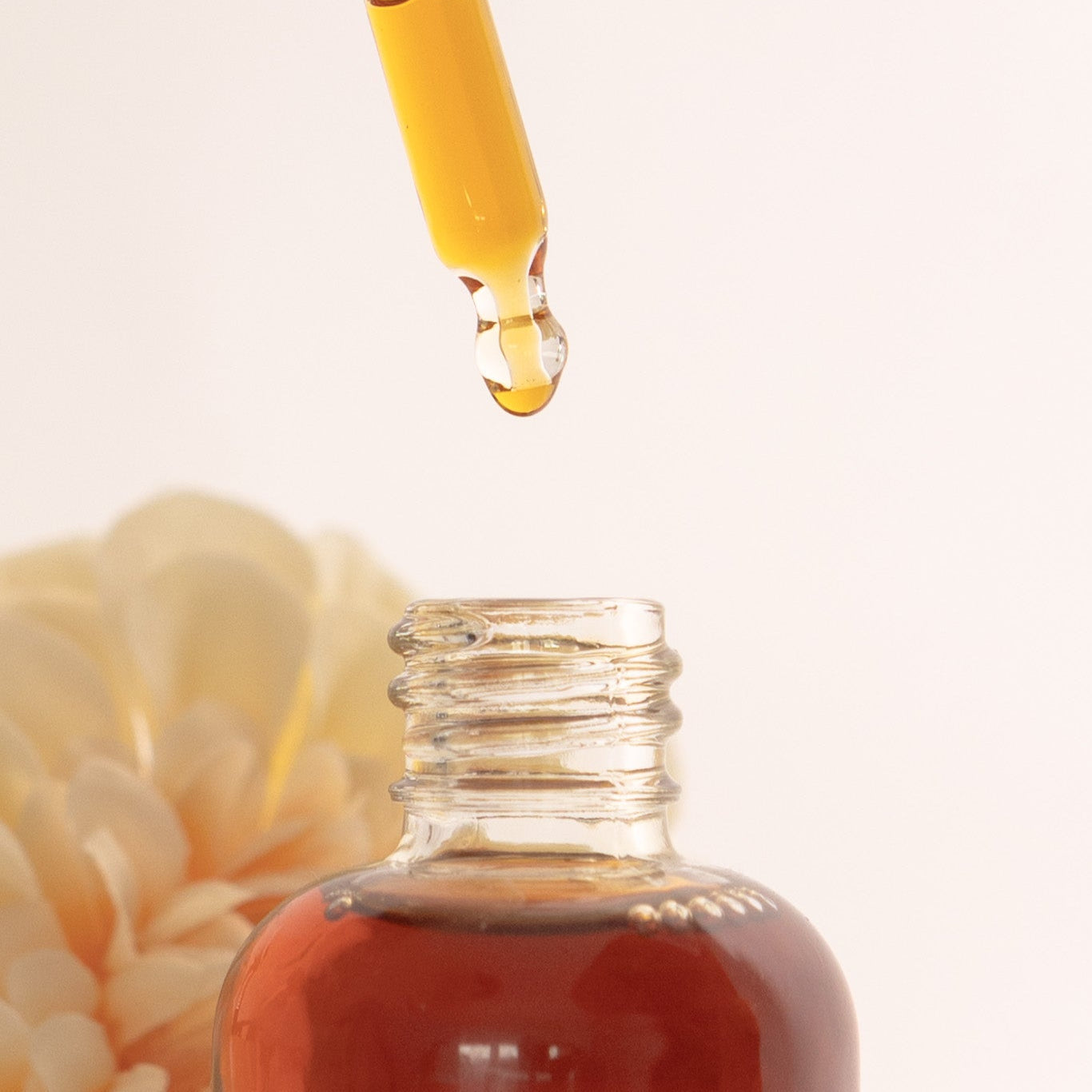 Glass dropper with yellow liquid over a glass bottle on a light background
