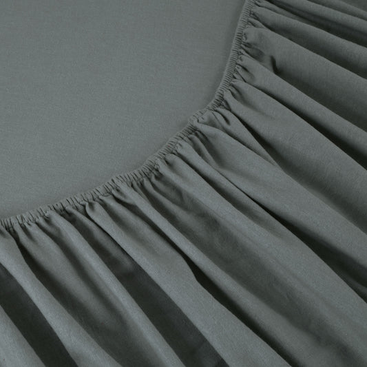 Gray bed sheets on a wooden bed with a wooden nightstand and decor items.