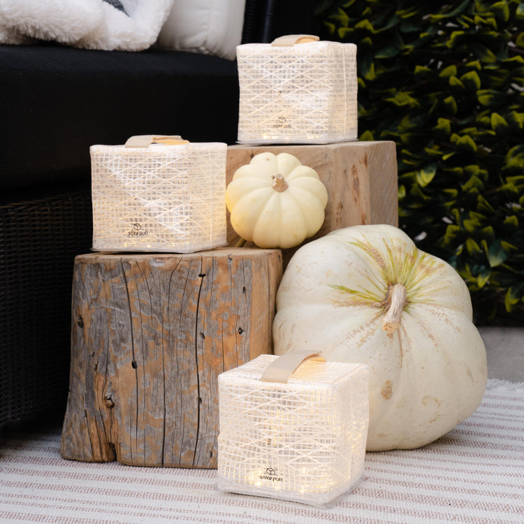 Decorative arrangement with candles and pumpkins on wooden blocks outdoors.