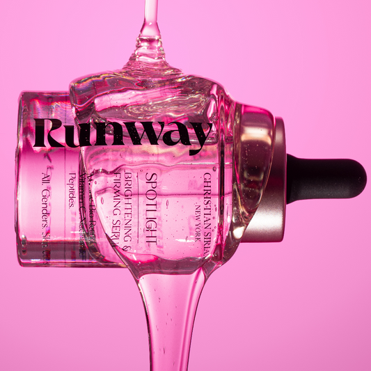 Christian Siriano Runway Spotlight Brightening Serum, clear glass bottle with dropper and clear liquid, featuring peptides, luxury skincare photo with vibrant pink backdrop.
