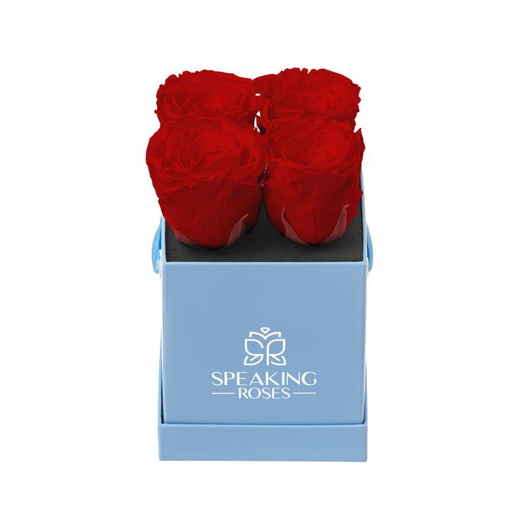 Four red roses in a blue box with 'Speaking Roses' logo on a white background